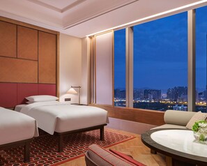 A hotel room with two beds, a sofa, a dining table, and a large window offering a city view. - ANDAZ XIAMEN, BY HYATT (Xiamen)