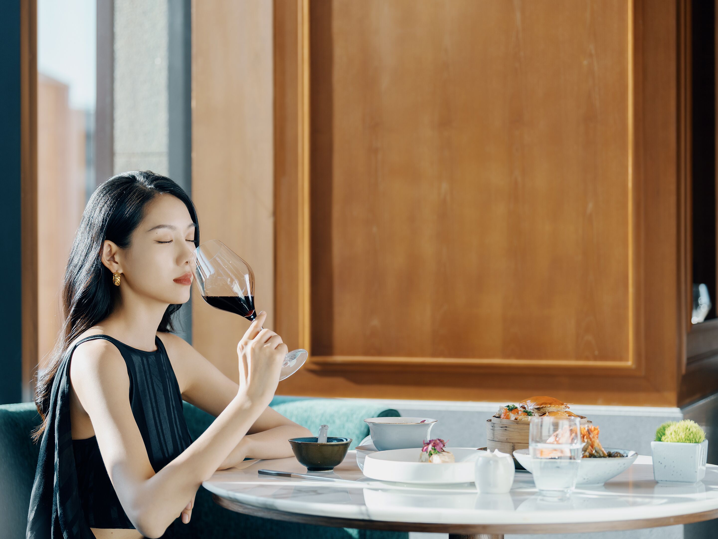 A person seated at a round table with a variety of dishes and a glass of red wine.