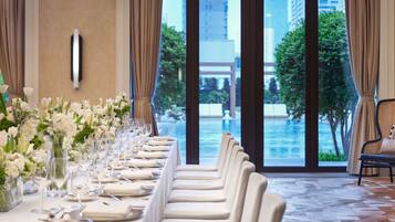 A long dining table set for a formal event with a view of a pool and buildings.