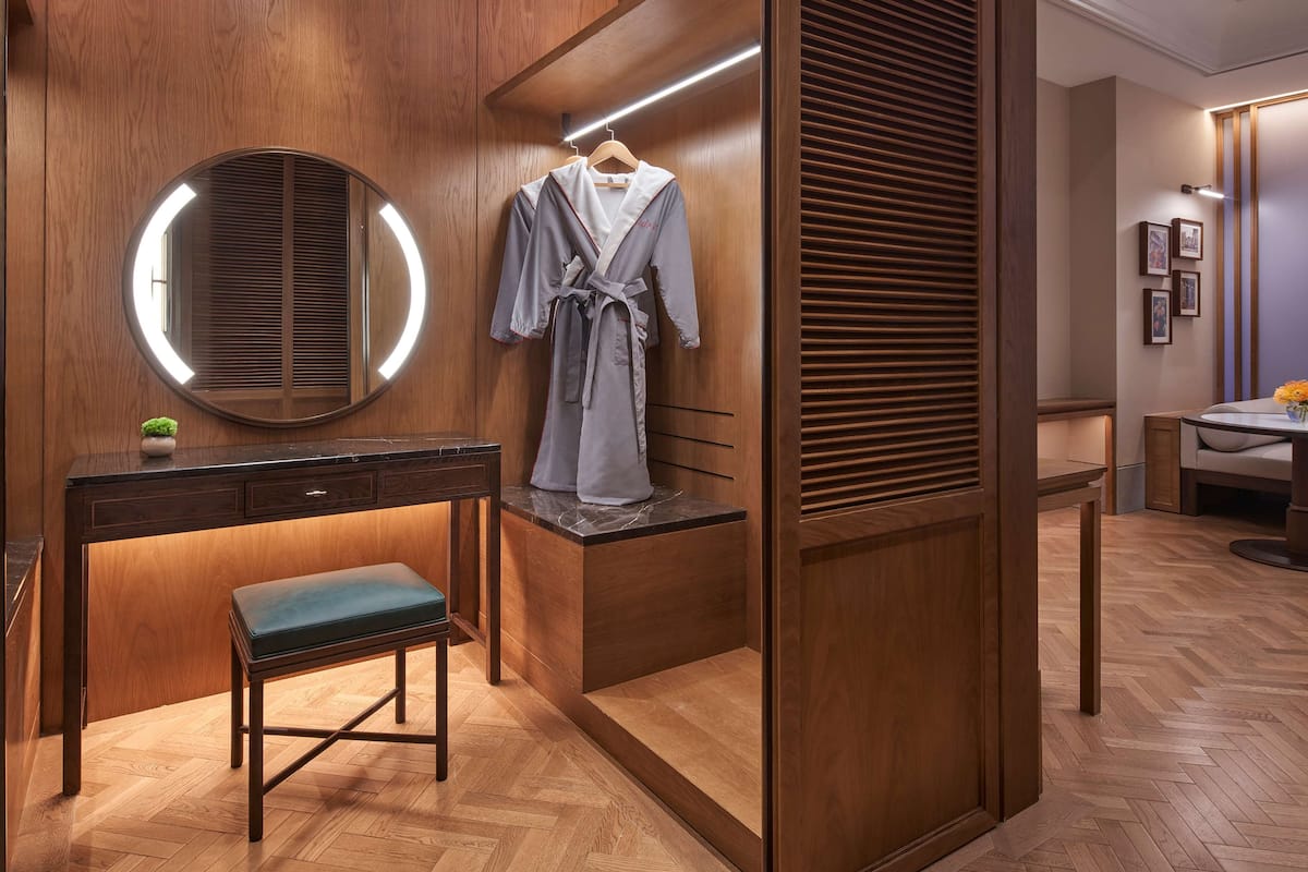 A modern bathroom with a wooden vanity, a round mirror, a robe hanging on the wall, and a bench.