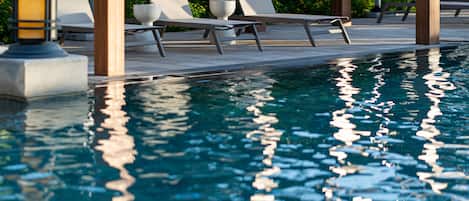 Una piscina al aire libre, sombrillas, sillones reclinables de piscina