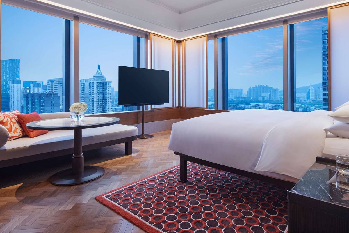 A hotel room with a large bed, a sofa, a TV, and a city view.
