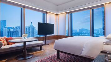A hotel room with a large bed, a sofa, a TV, and a city view.