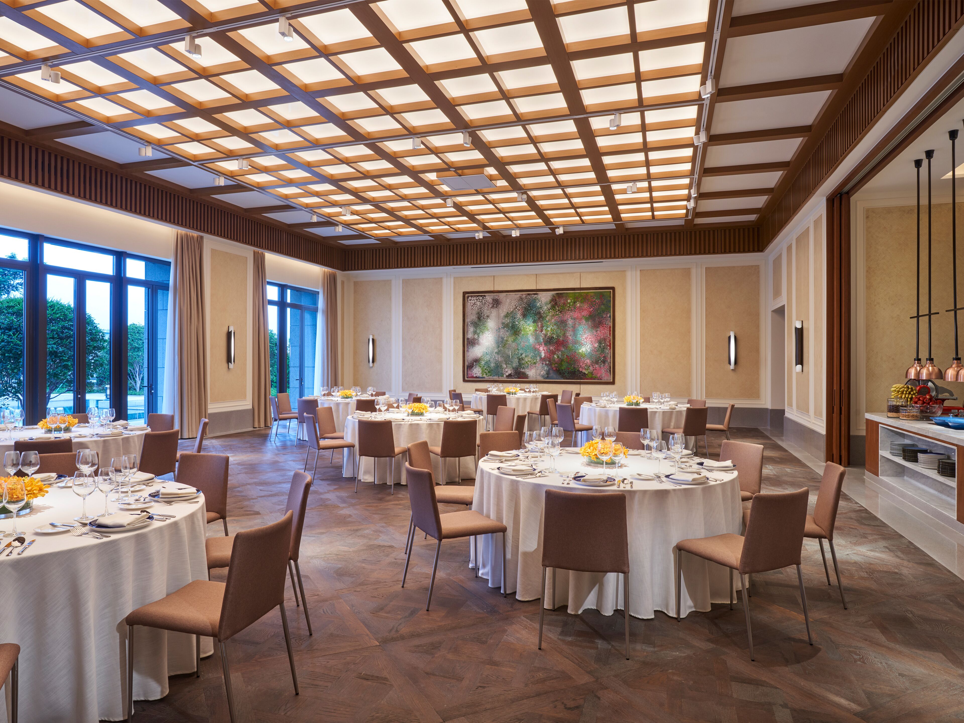 A spacious dining area with round tables, chairs, and a large window offering a view of the outdoors.