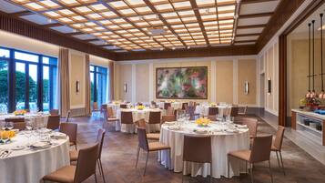 A spacious dining area with round tables, chairs, and a large window offering a view of the outdoors.