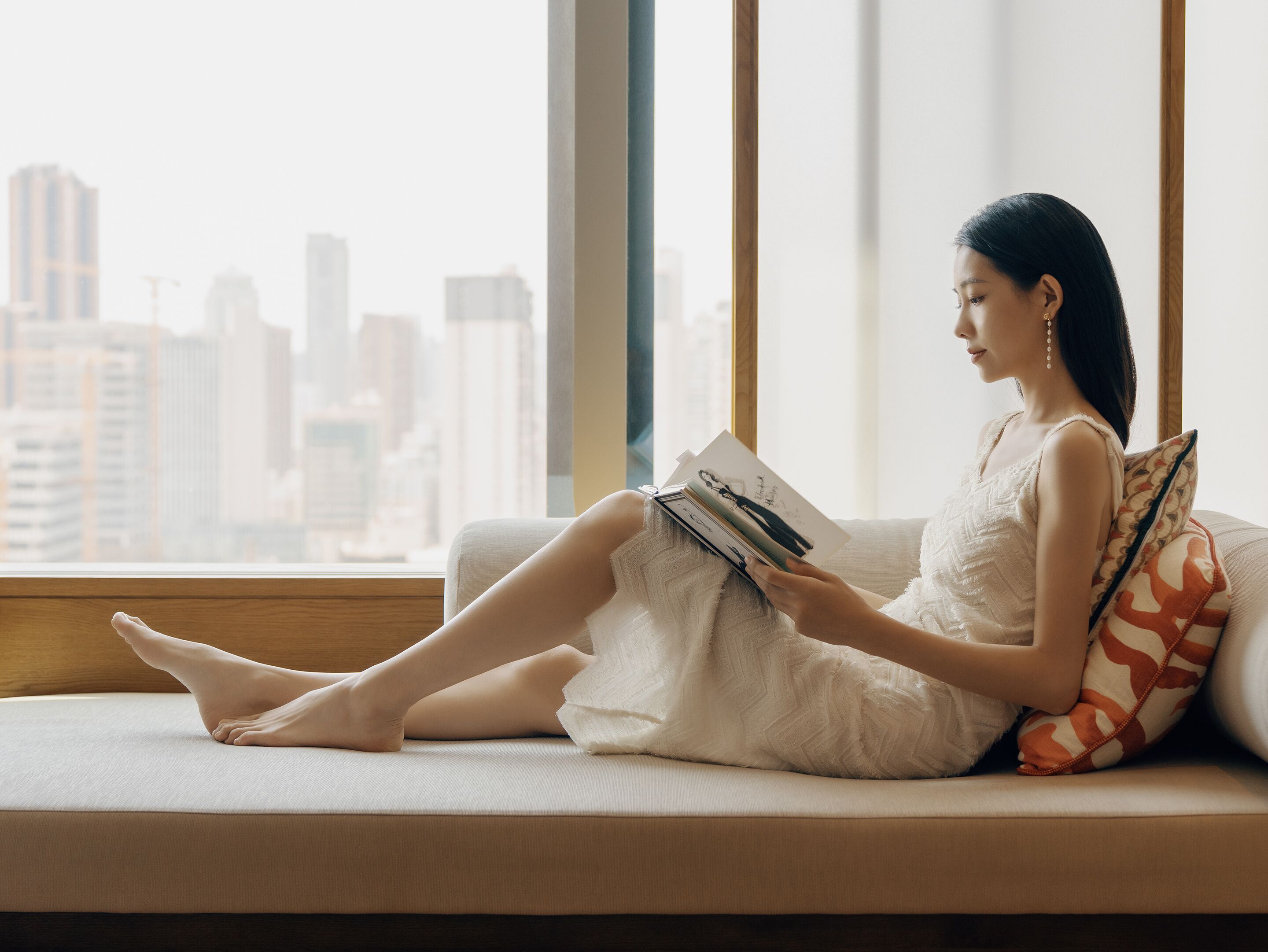 Una persona sentada en un sofá junto a una ventana con vista a la ciudad.