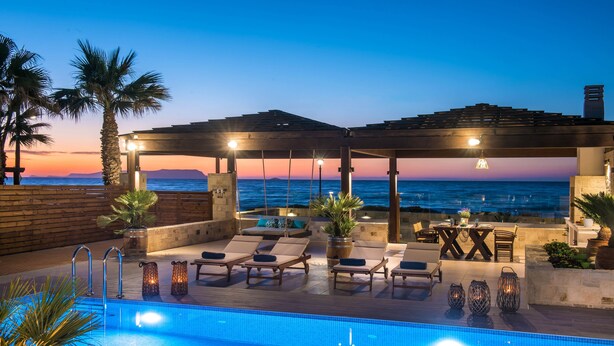 Ein Poolbereich mit Liegestühlen, einem Pool und Blick auf das Meer bei Sonnenuntergang.