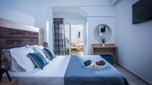 Ein modernes Schlafzimmer mit einem großen Bett, einem Nachttisch mit Obst und Kaffeetassen, einem Fernseher und einem wandmontierten Spiegel.