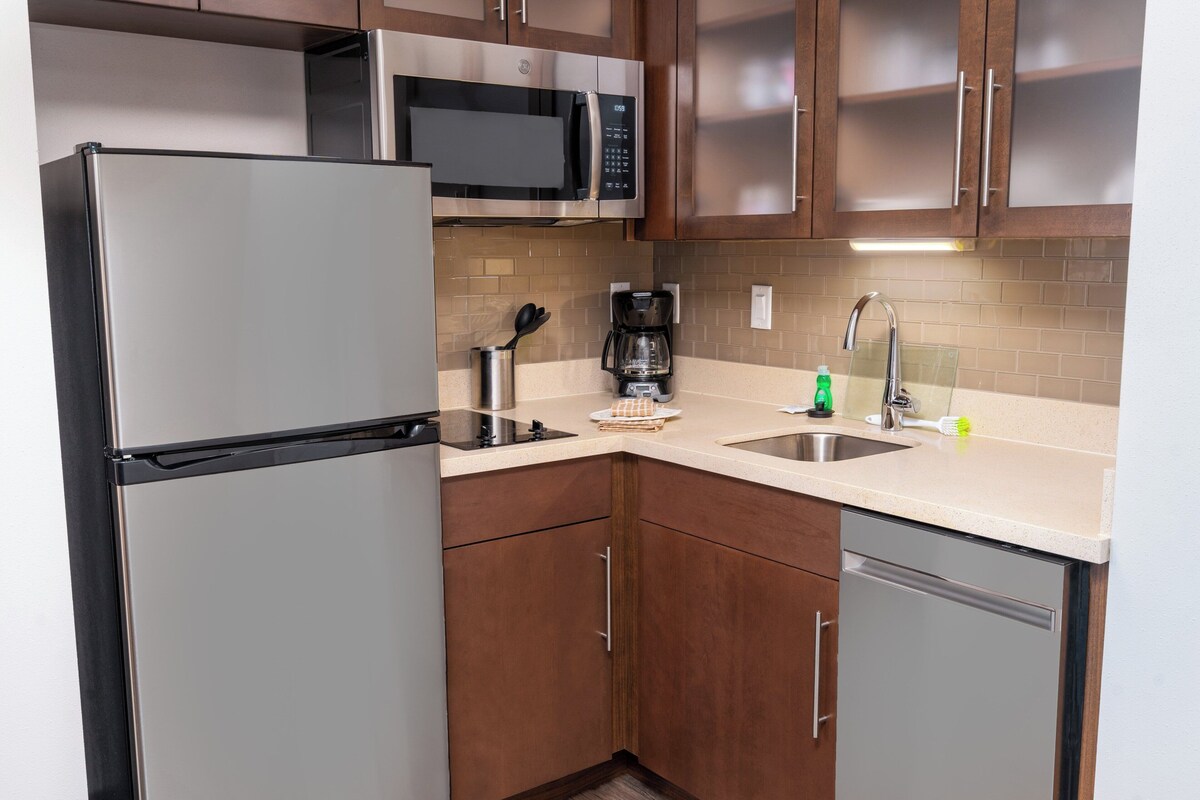 Cocina compacta equipada con refrigerador, microondas, cafetera, lavaplatos y fregadero.