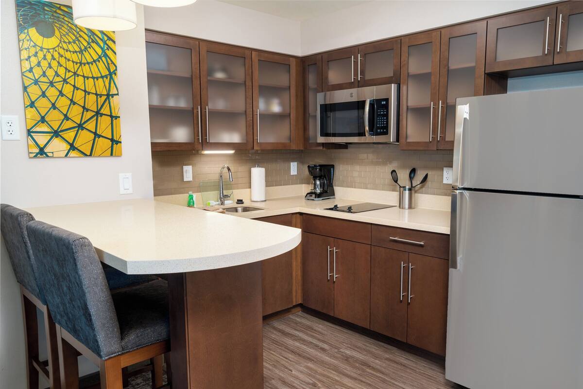 Una cocina con gabinetes de madera, un refrigerador de acero inoxidable, un microondas y una cafetera.