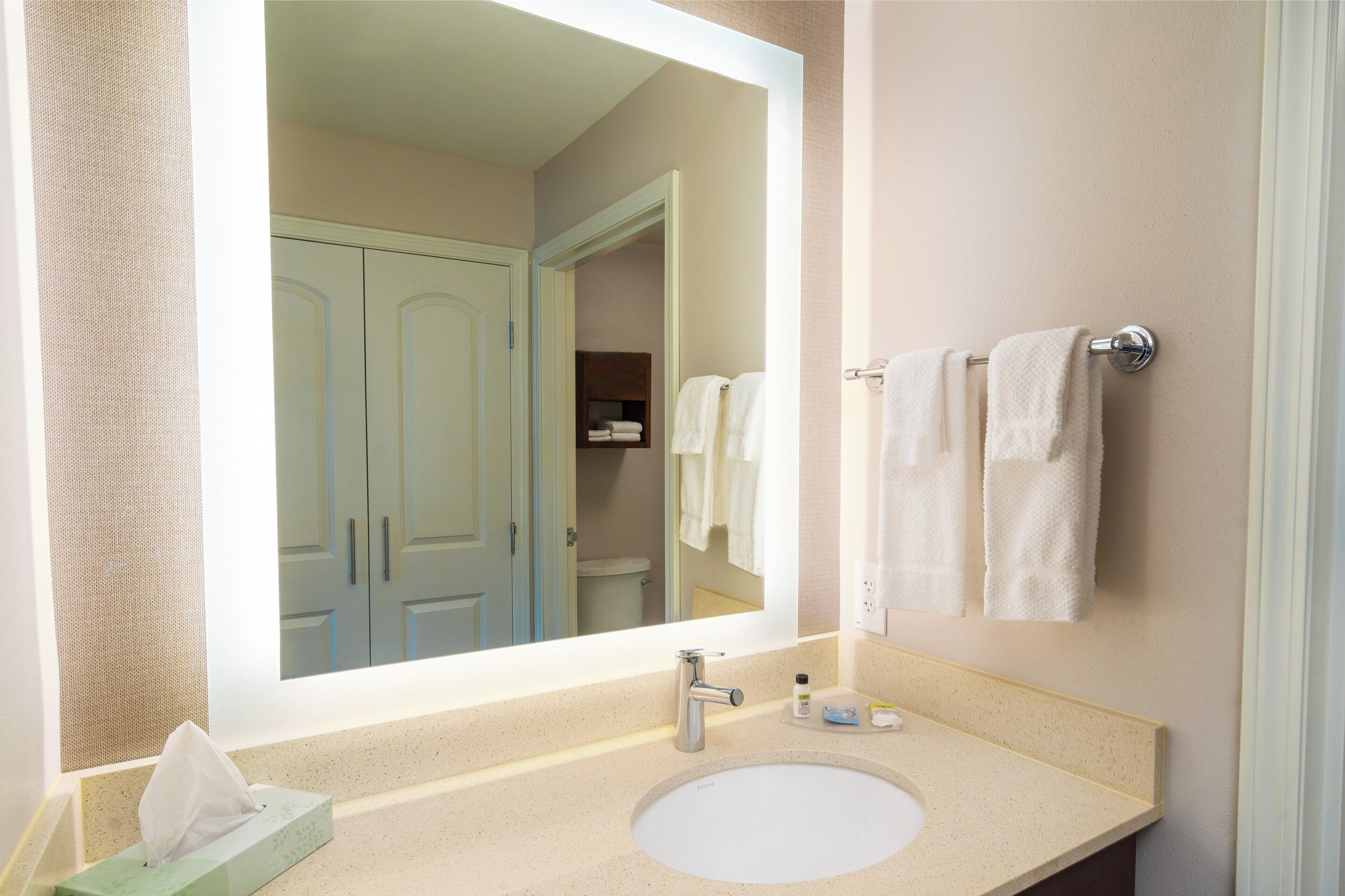 A bathroom with a large mirror, a sink, and a towel rack.