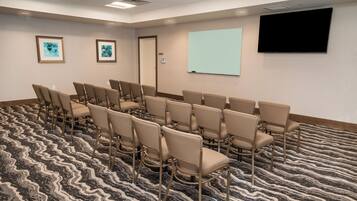 Une salle de conférence avec des rangées de chaises, un écran de projection et deux œuvres d’art encadrées accrochées au mur.