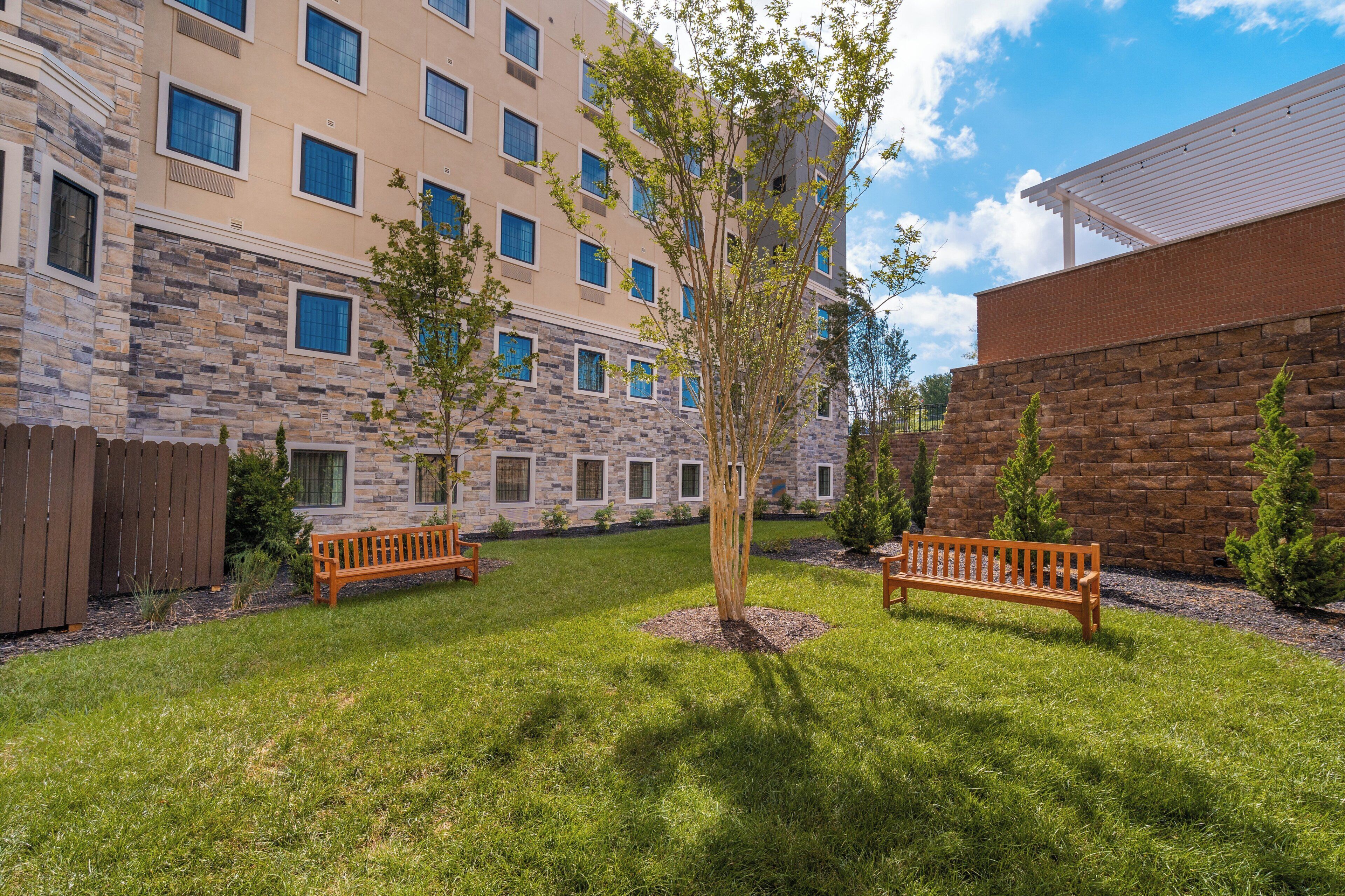 A courtyard with a stone building, two wooden benches, and a tree.