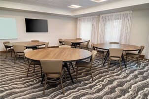 Un salón de conferencias con mesas redondas y sillas, una pantalla de proyector y alfombra estampada.