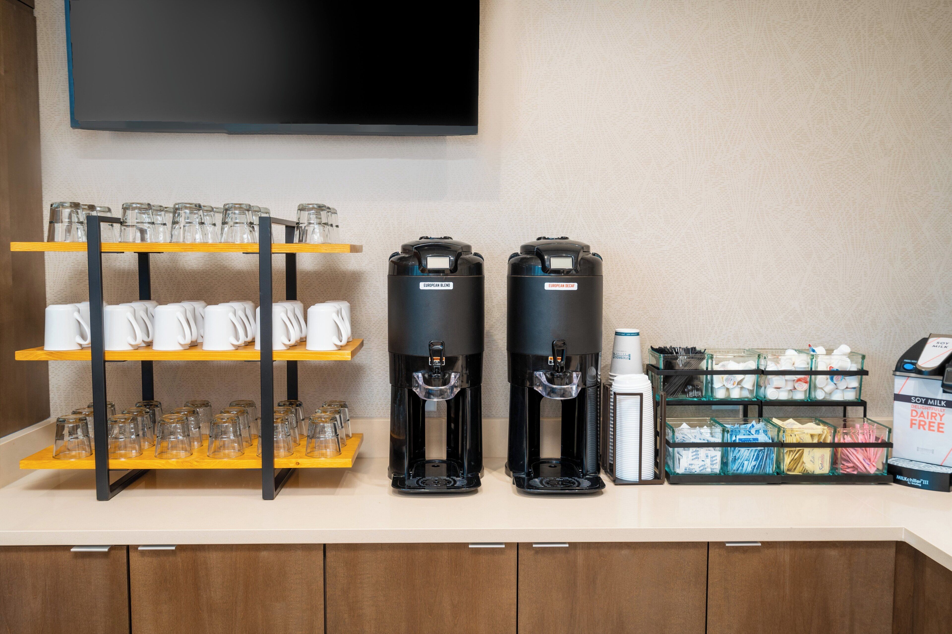 A coffee station with two dispensers, a glassware rack, and a milk dispenser.