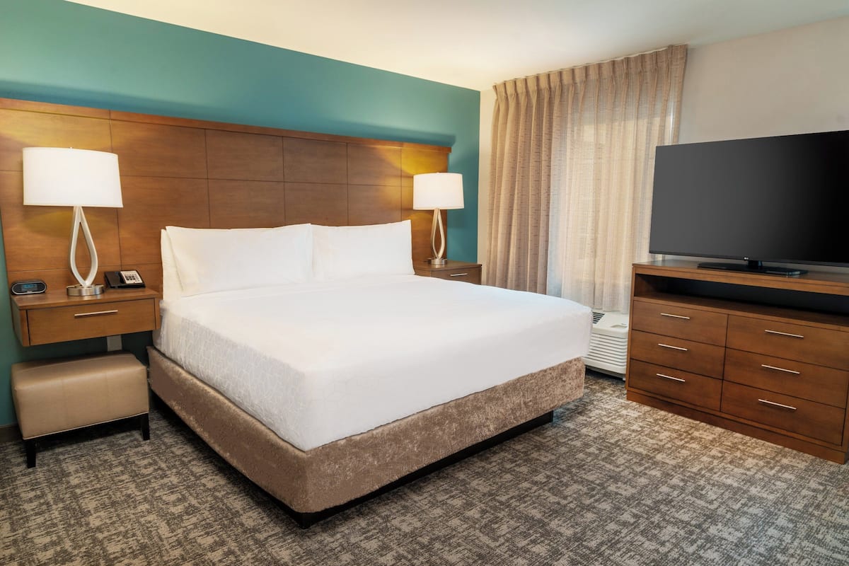 Una habitación de hotel con una cama grande, dos mesitas de noche con lámparas, un televisor y un armario.