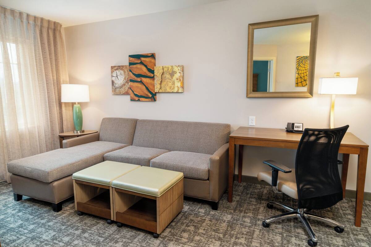 Habitación de hotel con sofá modular, escritorio, silla, lámpara y obras de arte en las paredes.