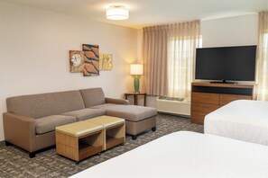 Une chambre d’hôtel avec un canapé, une petite table, une télévision, un lit et une lampe.