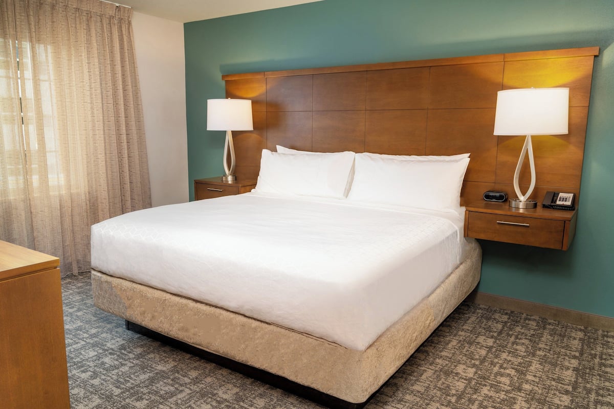 Habitación de hotel con una cama grande, dos mesitas de noche con lámparas, un cabecero de madera y piso alfombrado.