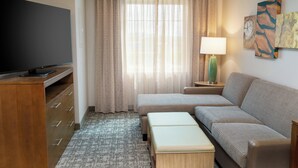 Een hotelkamer met een flatscreen televisie, een bank, een tafeltje, een lamp en kunst aan de muur.