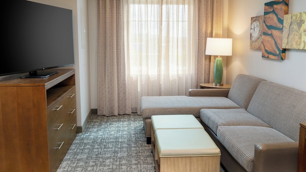 Une chambre d’hôtel équipée d’un téléviseur à écran plat, d’un canapé, d’une petite table, d’une lampe et d’œuvres d’art accrochées au mur.