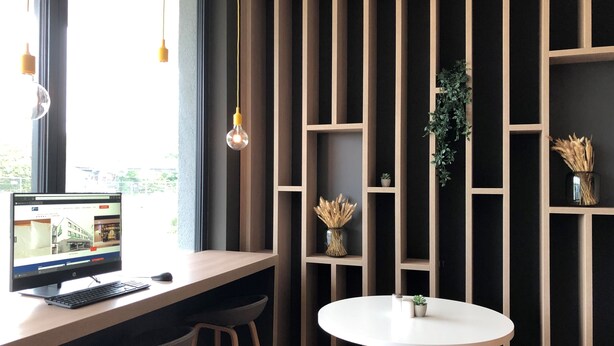 Et moderne arbejdsområde med en computer, to barstole, et rundt bord og en højreol med planter.