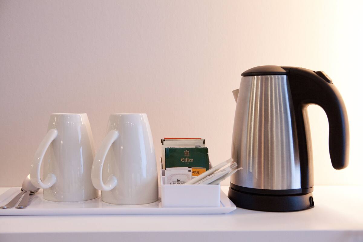 A white tray with two white mugs, a silver electric kettle, and a box of tea bags.