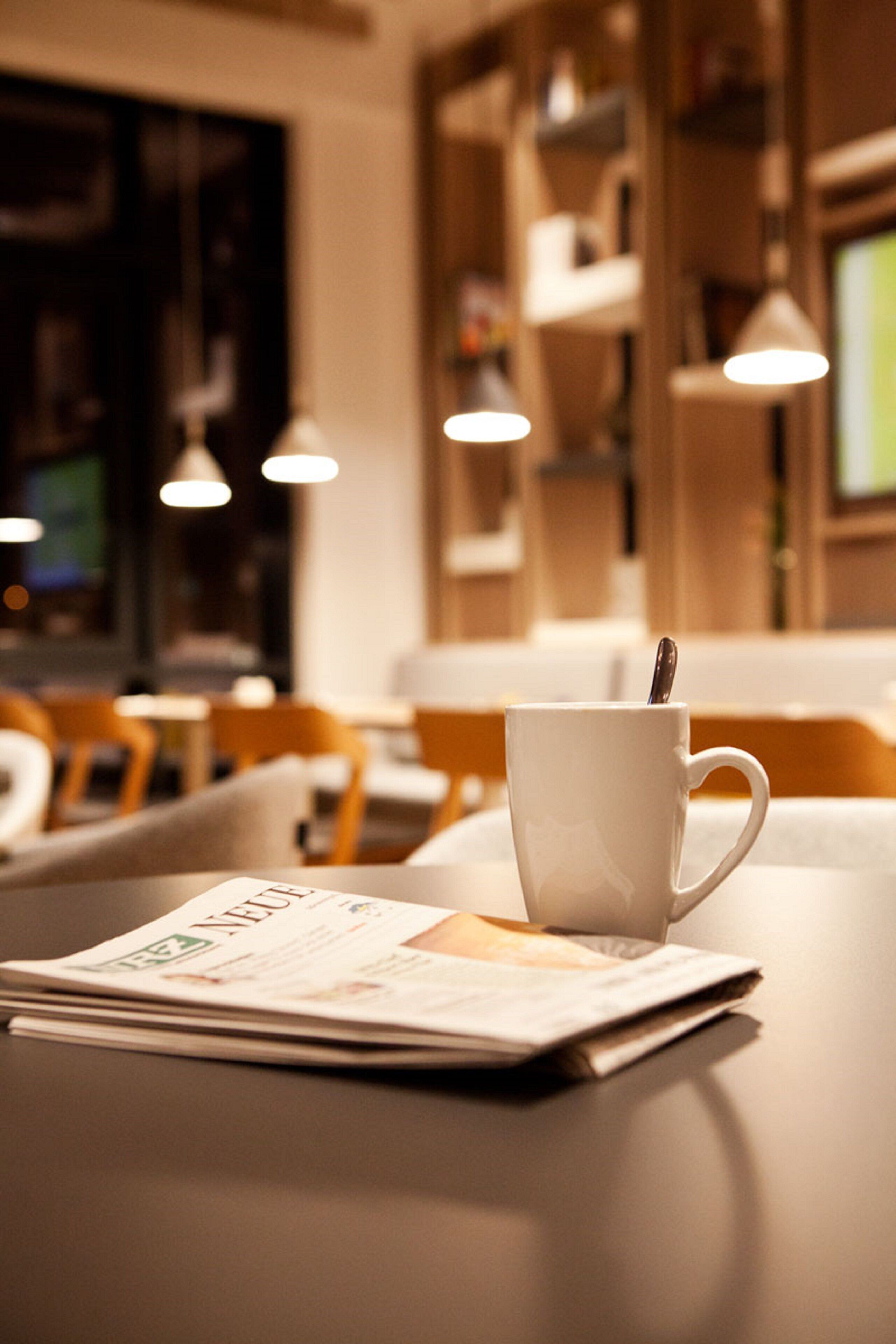 A white cup with a spoon on a table with a newspaper.