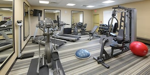A gym with treadmills, elliptical machines, a weight bench, dumbbells, and a red exercise ball.