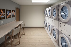 A laundry room with a long table and chairs, multiple washing machines, and artwork on the wall. - Candlewood Suites Odessa Midland by IHG (Odessa)