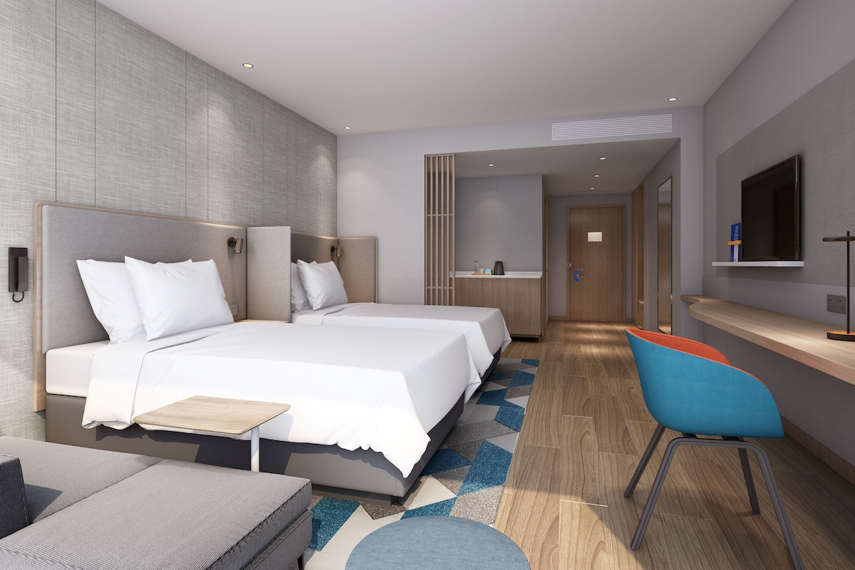 A modern hotel room with a large bed, a desk, a chair, and a television.