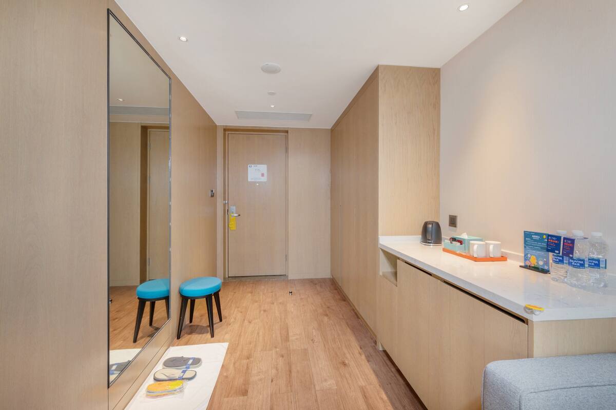 Hotelkamer met houten vloer, een spiegel, twee blauwe stoelen, een witte toonbank met toiletartikelen en een deur met een bordje.
