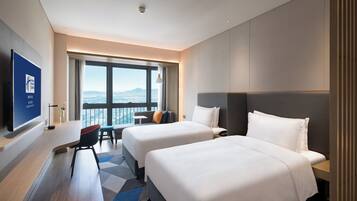 Habitación de hotel moderna con dos camas, un escritorio y un amplio ventanal con vistas a la ciudad.