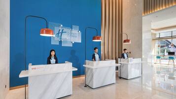 A hotel reception area with marble counters, a blue textured wall, and modern pendant lighting.