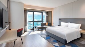 Une chambre d’hôtel moderne dotée d’un grand lit, d’un bureau, d’une chaise et d’un balcon offrant une vue sur les montagnes.