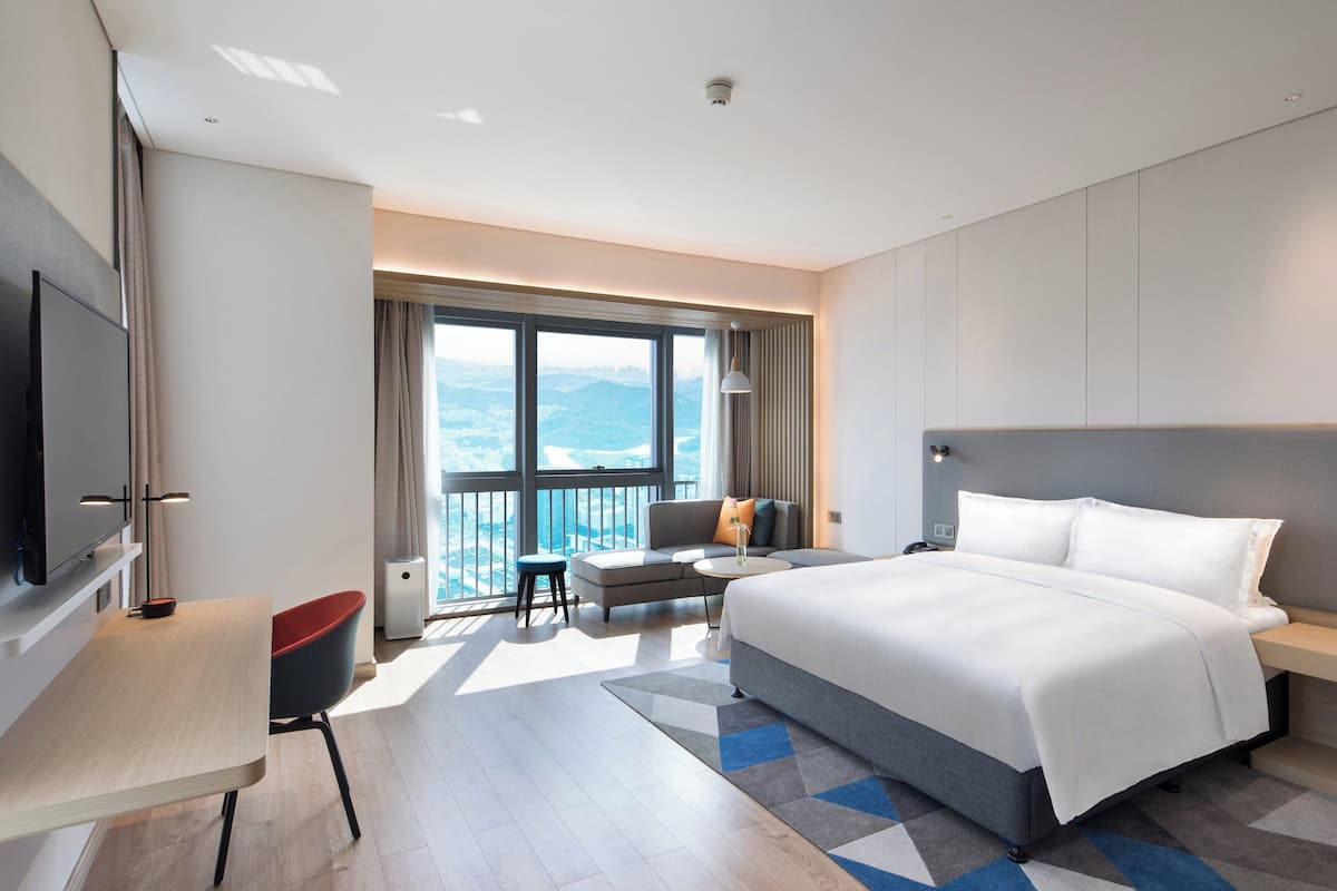 Een moderne hotelkamer met een groot bed, een bureau, een stoel en een balkon met uitzicht op de bergen.