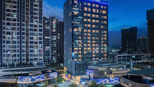 Un hôtel de grande hauteur doté d’une façade moderne en verre, d’une enseigne lumineuse et d’une terrasse sur le toit agrémentée d’un éclairage extérieur.