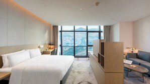 Une chambre d’hôtel dotée d’un grand lit, d’un canapé, d’un bureau et offrant une vue sur le paysage urbain grâce à de grandes fenêtres.