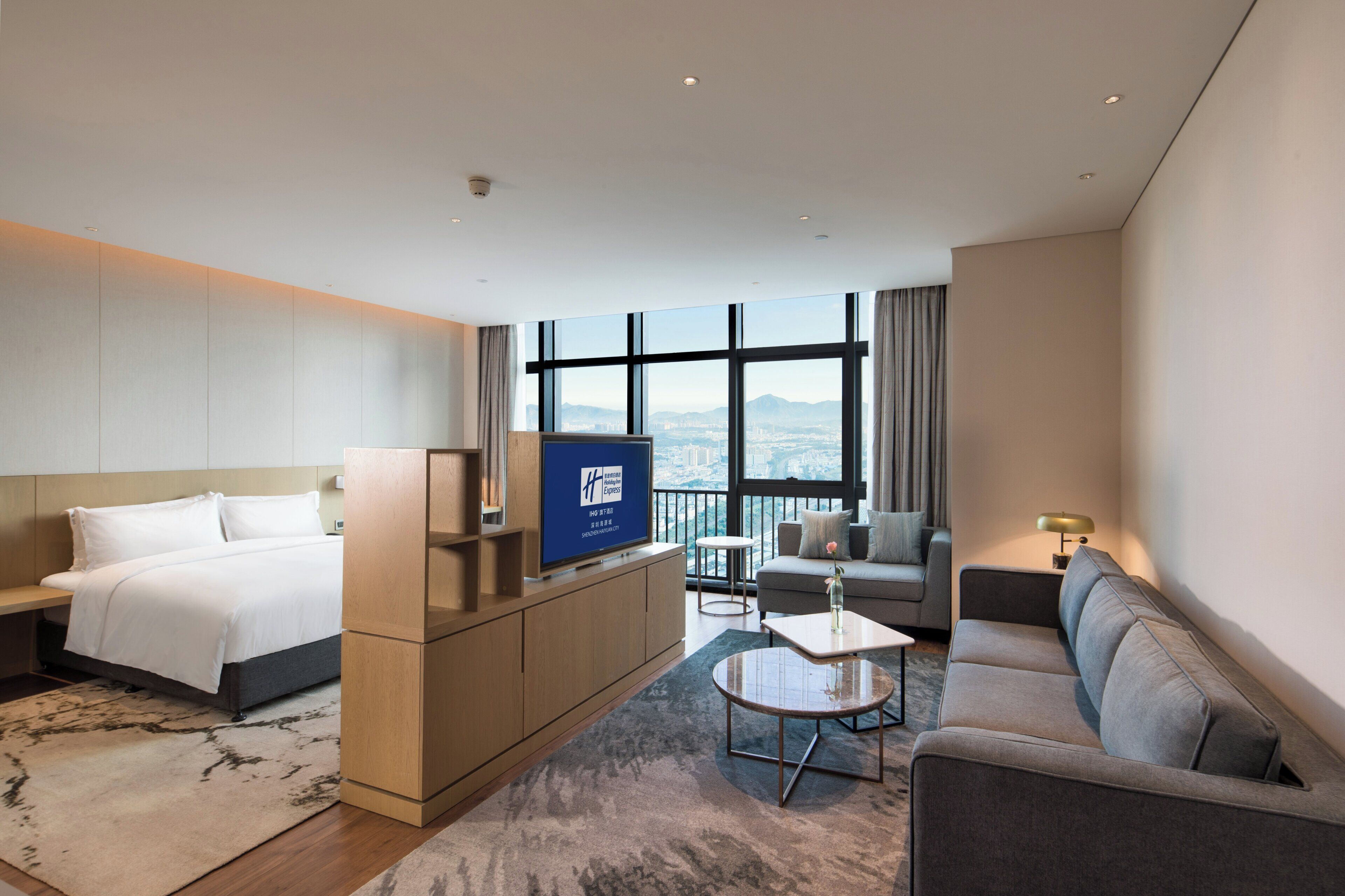 Habitació d'hotel amb un llit, un sofà, una taula petita, una televisió i vistes a la ciutat.