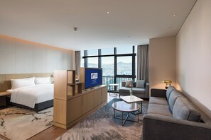 Camera d'albergo con un letto, una poltrona, un tavolino, una TV e vista sulla città.