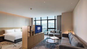 Une chambre d’hôtel moderne équipée d’un lit, d’un canapé, d’une télévision et offrant une vue sur la ville grâce à de grandes fenêtres.