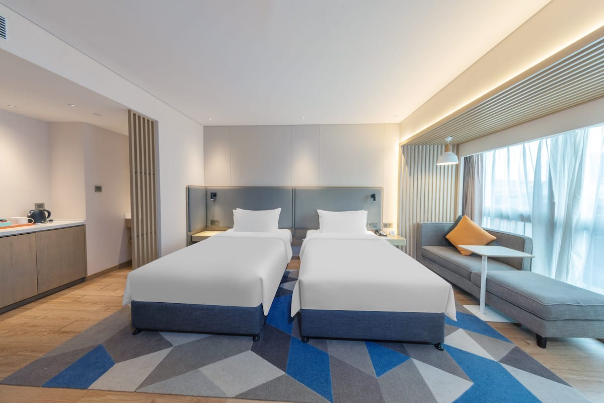 Een moderne hotelkamer met twee bedden, een bank, een tafeltje en uitzicht op de stad.
