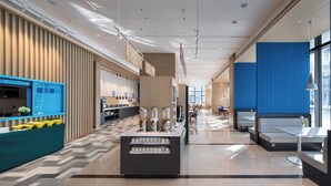 Un hall d’hôtel moderne avec un comptoir d’accueil central, des espaces de détente et une cuisine visible au fond.