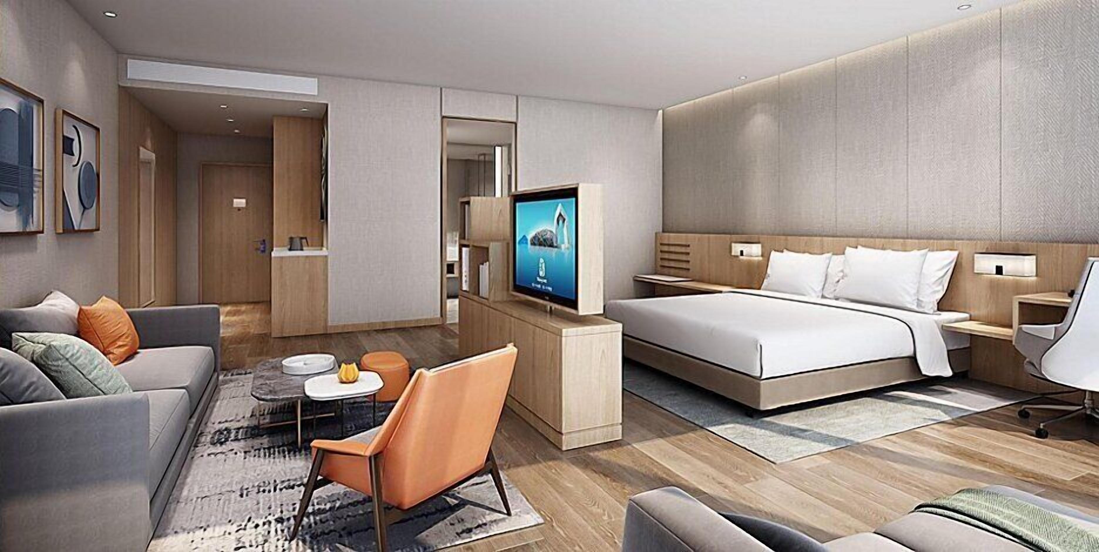 A modern hotel room with a bed, a sofa, a desk, a TV, and a chair.