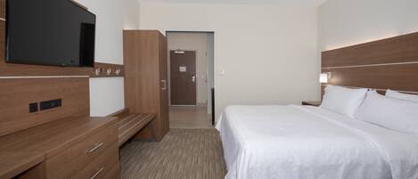 A hotel room with a bed, a TV mounted on the wall, a wooden dresser, and a door leading to another room.