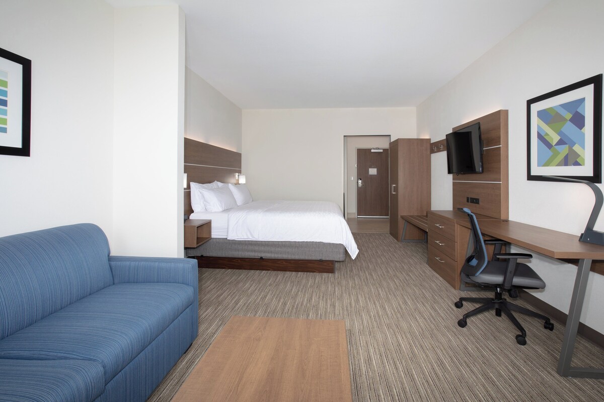 A hotel room with a bed, a desk with a chair, a sofa, and a television.