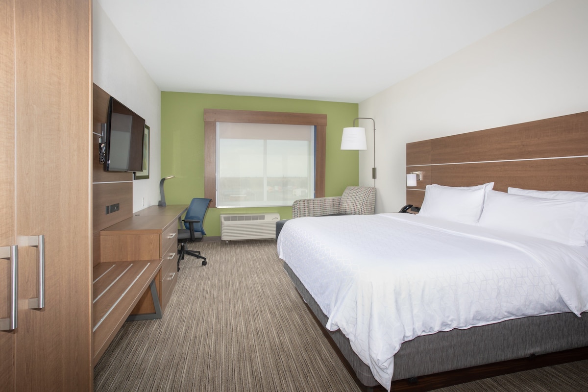 Quarto de hotel com cama, escrivaninha, cadeira e televisão.