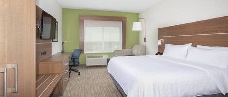 Quarto de hotel com cama, escrivaninha, cadeira e televisão.