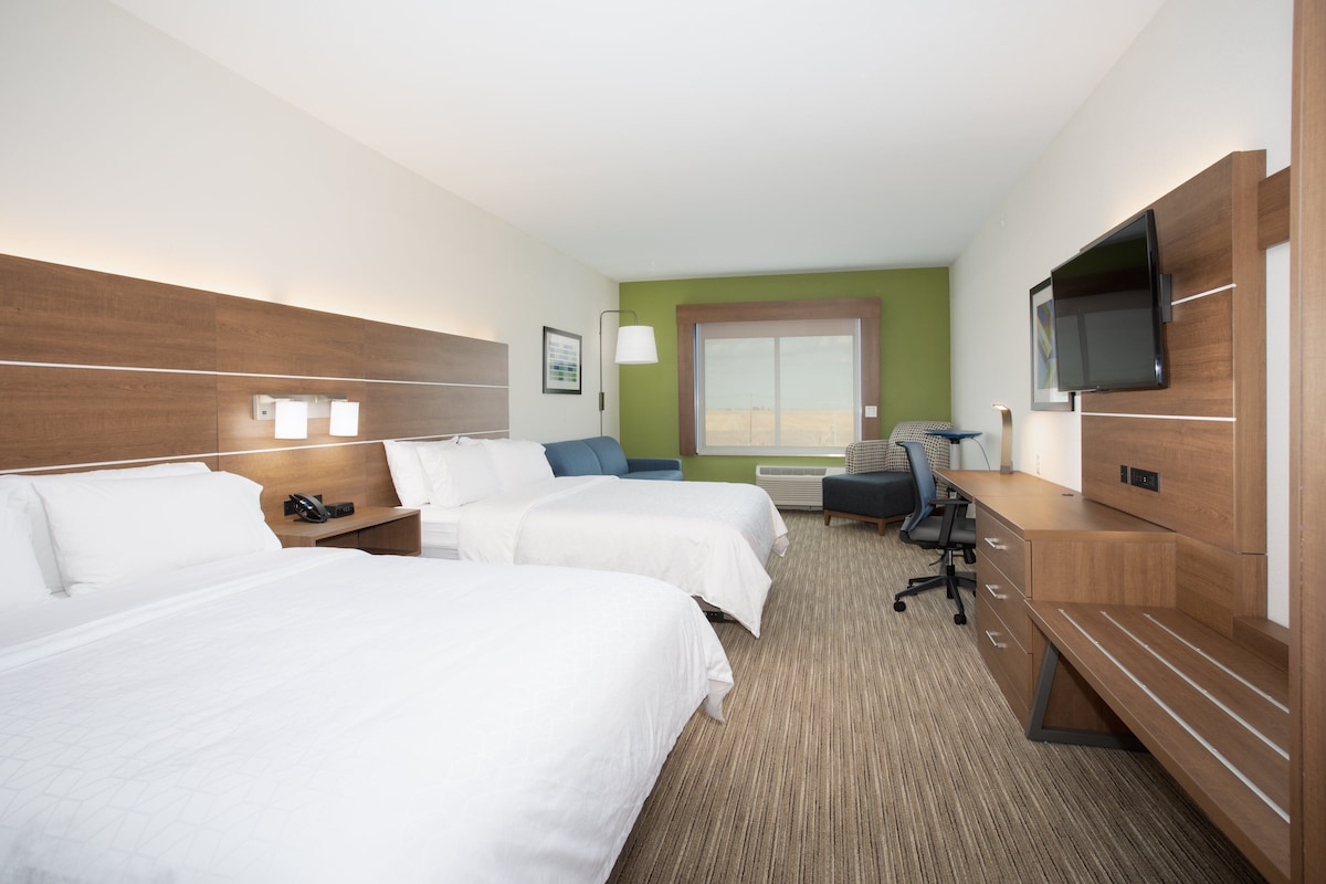 Quarto de hotel com duas camas, uma escrivaninha, uma cadeira, uma televisão e uma janela.