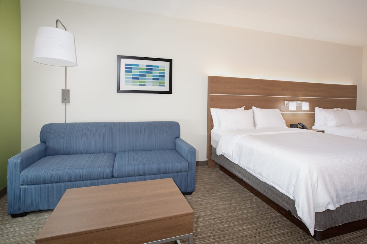 Una habitación de hotel con una cama, un sofá azul, una mesa de madera, una lámpara de pie y un cuadro en la pared.